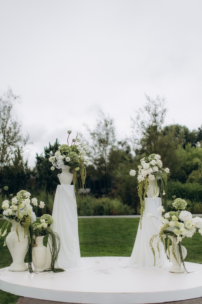 Décoration Florale Mariage Extérieur : Blanc et Vert Décoration de mariage élégante avec fleurs blanches et vertes sur colonnes drapées lors d'une cérémonie en extérieur.